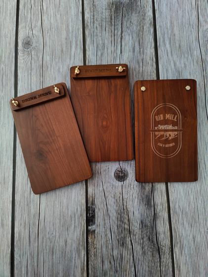 Three walnut wood menu clipboards with engraved header strips and laser engraved logo, on grey wood, custom made by RestroCart, New Delhi