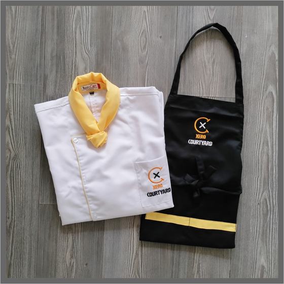 White chef coat with yellow collar and black bib apron with yellow hem band and logo, custom made for Xero Courtyard by RestroCart, New Delhi