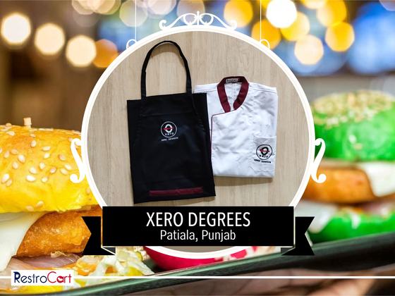 Black bib apron with logo beside a white chef coat with maroon collar, laid flat, custom made for Xero Degrees by RestroCart, New Delhi