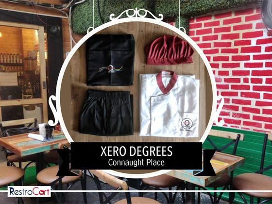 White chef coat with maroon collar, maroon cap, black apron and trousers, laid out as a set, custom made for Xero Degrees by RestroCart, New Delhi